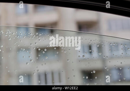 Le gocce di pioggia sulla vettura verso la parte anteriore del vetro laterale Foto Stock