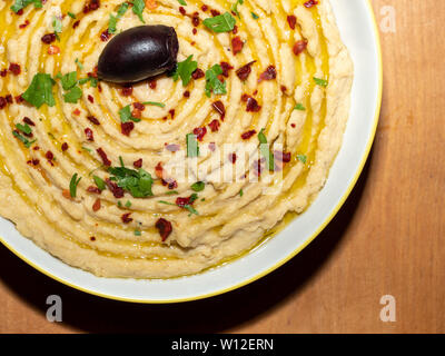 Hummus - Oriental antipasto - pasta di ceci in una ciotola su una tavola di legno, guarnite con prezzemolo, pepe, olio d'oliva Foto Stock