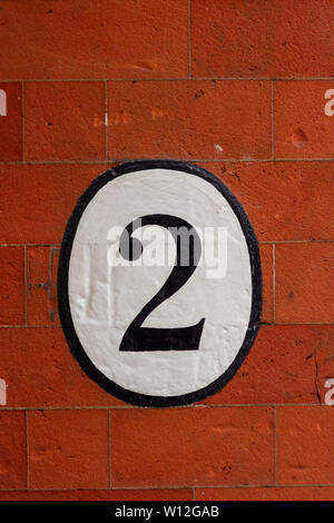 Casa numero due con il 2 dipinta in un ovale su un rosso muro di mattoni Foto Stock