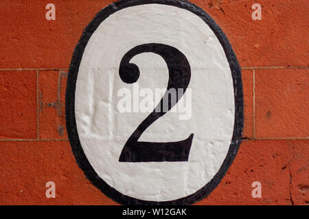 Casa numero due con il 2 dipinta in un ovale su un rosso muro di mattoni Foto Stock
