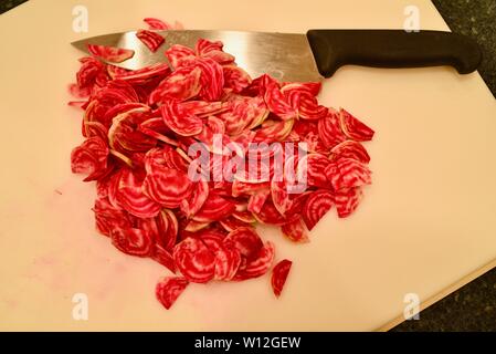 Tagliate a fette, fattoria fresco, rosso brillante chioggia bietole (barbabietole) su un bianco tagliere con coltello, Wisconsin, Stati Uniti d'America. Foto Stock