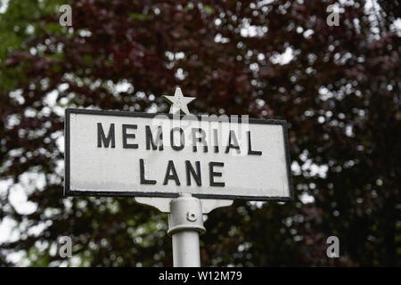 Lettere in nero su bianco paint Memorial Lane segno sulla parte superiore di un montante con una stella sulla parte superiore con il rosso scuro albero a foglia sfondo bokeh di fondo in Falmouth, Massachusett Foto Stock