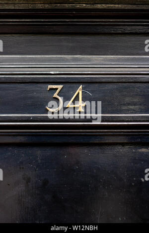 Casa numero 34 con trentaquattro in cifre di metallo su una tavola di legno porta anteriore Foto Stock