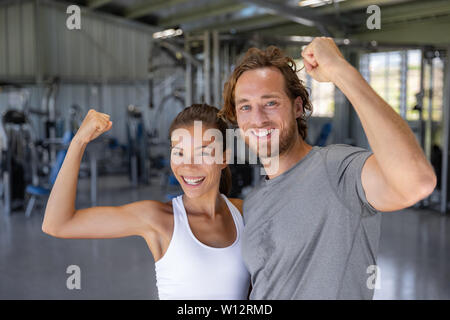 Montare la potenza coppia felice flessione forti braccia in mostra il successo della formazione a una palestra per il fitness - sorridente donna asiatica, uomo caucasico . Foto Stock