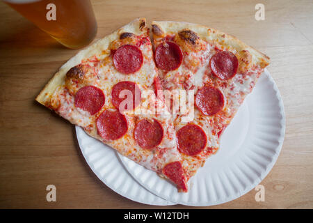 Due fette di salsiccia per pizza pizza su una piastra con una birra Foto Stock