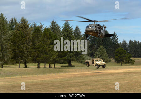 Un UH-60 Black Hawk si prepara a sollevare un militare di elevata mobilità multiuso di veicolo a ruote durante Air Assault della formazione di Camp Rilea, Warrenton, Oregon, 27 giugno 2019. (Guardia Nazionale foto da John Hughel, Oregon Dipartimento militare federale degli affari pubblici) Foto Stock