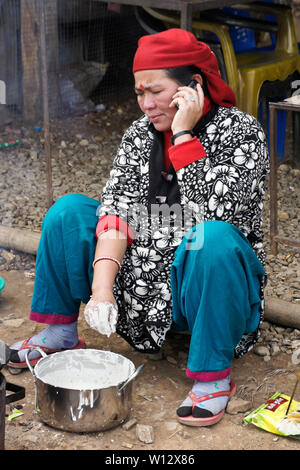 Donna in abito tradizionale parlando al telefono cellulare mentre si effettua la sel (impasto fritto) presso un ristorante su strada nelle zone rurali del Nepal Foto Stock