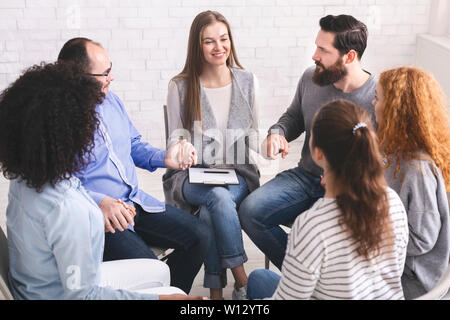 Diverse persone seduti su sedie in cerchio tenendo le mani Foto Stock