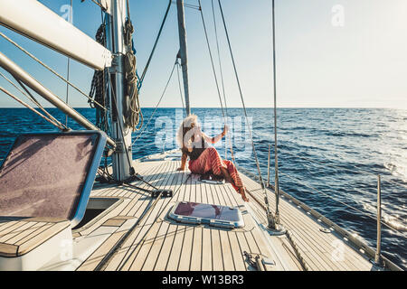 Le persone godono di avventura di viaggio con mezzi di trasporto alternativi - Via Ricci bella donna bionda sedersi su una barca a vela con oceano e cielo intorno a - e Foto Stock