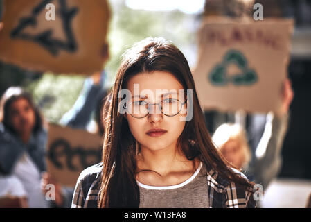 Giovane donna in eyewear con gruppo di dimostranti femmina tenendo la segnaletica permanente, mentre all'aperto sulla strada. Concetto di ecologia. Gruppo protestando Foto Stock