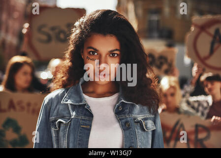 Forza delle donne. Afro American donna con la parola scritta di potenza sul suo viso protestando con gruppo di attivisti femmina all'aperto sulla strada. Diritti dell'uomo. Dimostrazione Foto Stock