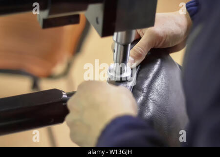 Macchina in un workshop in pelle in azione con le mani lavorando con dettagli in pelle per borse o scarpe. Artigianali in pelle. Foto Stock