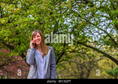 Giovane donna sorridente e ascoltare il suo telefono in un parco. Foto Stock