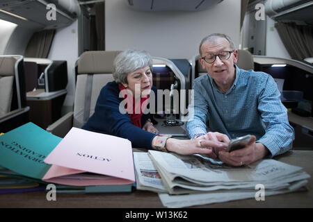 Il primo ministro Theresa Maggio guarda le foto del Vertice G20 presi da suo marito, Filippo come essi volare indietro dalla riunione dei leader mondiali di Osaka in Giappone. Foto Stock