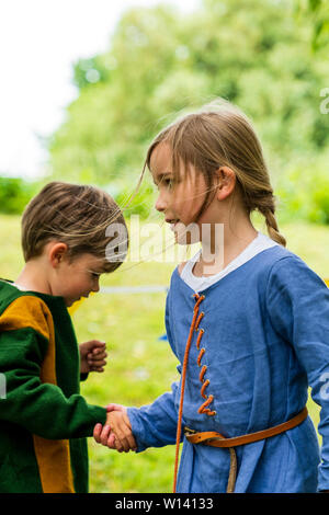 Due bambini, boy, 3-4 anni, e una ragazza, 5-6 anni, vestito in abiti medievali, tenendo le mani che corre intorno a ogni altro. Foto Stock