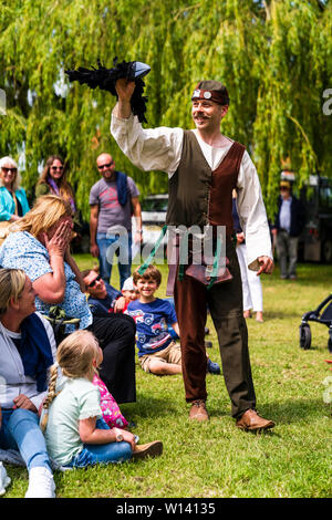 Rievocazione evento. Teatro medievale, all'aperto, uomo, mummer o player, tenendo in mano un corvo nero puppet durante l'esecuzione di un gioco per adulti e bambini. Foto Stock