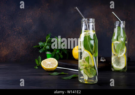 Freschi cocktail mojito bevande in bottiglie e ingredienti, limone e menta in gronda bascet su sfondo scuro, cocktail bibite estive concept Foto Stock