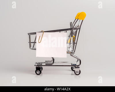 Carrello spesa e white paper nota elenco isolato su sfondo bianco. Il concetto di shopping su luce sfondo monocromo. Vuoto di carta bianca nota su carrello. Copia spazio per il testo o il design. Foto Stock