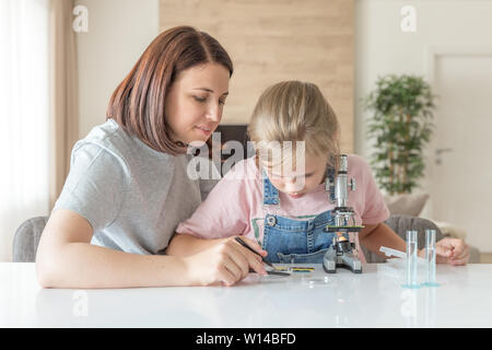 Madre e figlia giovane a fare alcuni esperimenti con microscopio a casa Foto Stock