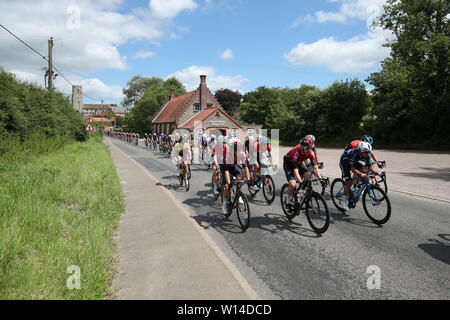 Gli uomini delle élite Peloton passa attraverso il villaggio di Hindringham durante il British Ciclismo Campionati Nazionali di corsa su strada attraverso Norfolk. Foto Stock