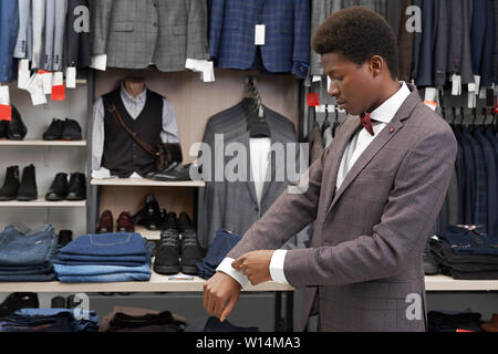 Giovane uomo, African cercando su elegante abito grigio, guardando il manicotto. Fiducioso client di boutique alla moda in camicia bianca con fiocco rosso giacca e cravatta Foto Stock