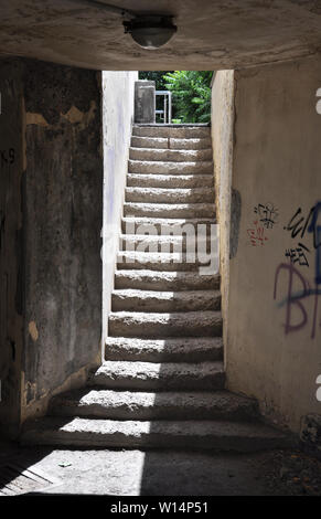 Il passaggio ascendente dalla zona della metropolitana con la luce del sole di contrasto al piano di sopra, weathered passaggi stretti e sporca le pareti in calcestruzzo Foto Stock