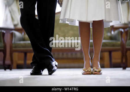 Gambe di lo sposo in nero scarpe e pantaloni e spose in beige tacchi con snow-orlo bianco di un abito da sposa Foto Stock