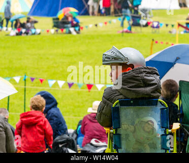 Linlithgow Palace, West Lothian, Scozia, Regno Unito, 30 giugno 2019. Giostre a Linlithgow Palace: ambiente storico Scozia presente la loro annuale famiglia medievale giornata di divertimento presso la buccia. L'evento principale è una spettacolare giostre e equitazione display dall'equino team stunt Les amis d'Onno. Un ragazzo che indossa un casco medievale si siede su una sedia in attesa della giostra per iniziare Foto Stock