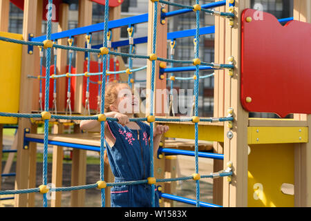 Ragazza adolescente cerca di arrampicarsi sulla parete della fune. Lei sta giocando con la corda parete per sviluppare attività motoria presso il parco giochi Foto Stock