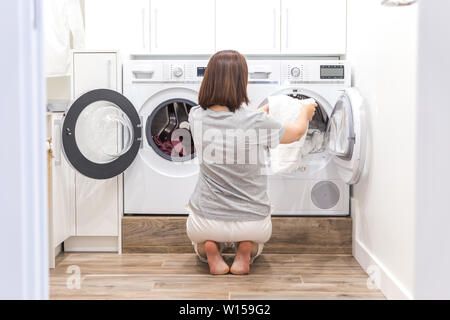 Donna di mettere i vestiti per macchina di lavaggio per lavare Foto Stock