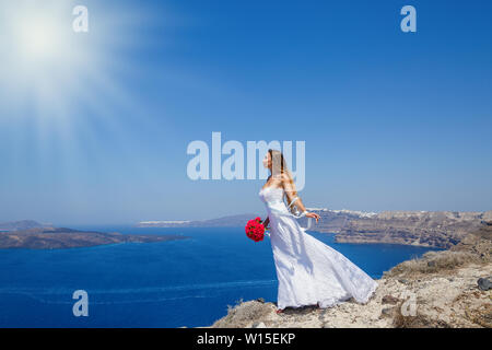 Bella ragazza in un abito bianco sorge su una scogliera e guarda al mare, la Grecia, l'isola di Santorini. Foto Stock