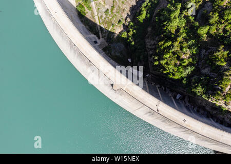 Serbatoio acqua Lac de Emosson, verticale drone shot della diga muro, persone che camminano nella diga, Lac d'Emosson, canton Vailais, Vallese, Svizzera. Foto Stock