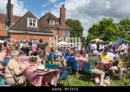 Un sacco di persone godendo di tè, bancarelle e intrattenimento a un villaggio inglese estate fete (fayre) in una giornata di sole in giugno Foto Stock