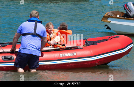 Padre getting in gomma gonfiabili con due bambini piccoli in giubbotti di salvataggio off testata est, porto di Chichester, West Sussex, in Inghilterra, Regno Unito Foto Stock