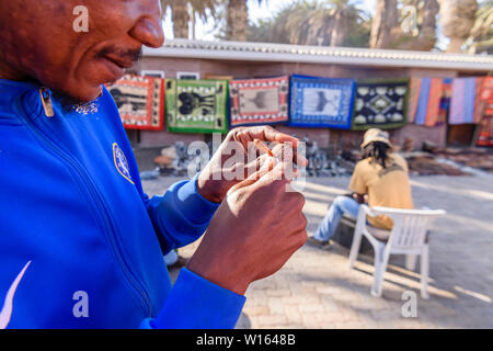 Tobias scolpisce piccoli souvenir in legno con i nomi dei turisti in Swakopmund craft market, Namibia. Foto Stock