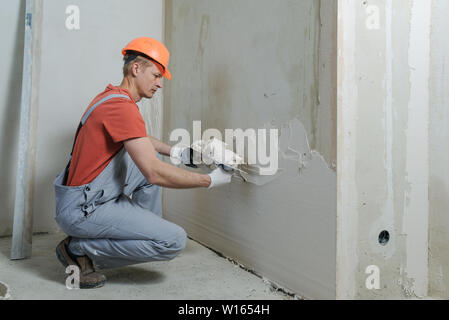 Lavoratore è mettere un gesso su una parete. Egli è con una cazzuola a lungo. Foto Stock