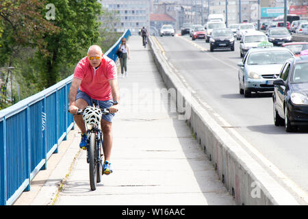 Belgrado, Serbia - Aprile 25, 2019: persone equitazione mountain bike e passeggiate sulla corsia separata sulla strada di città ponte affollato Foto Stock