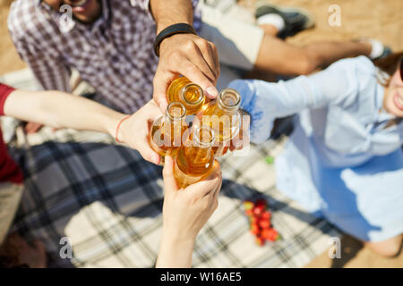 Sopra Visualizza Ingrandimento delle mani il tintinnio di bottiglie di birra contro il cielo blu in estate, spazio di copia Foto Stock