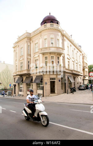 Belgrado, Serbia - Aprile 26, 2019: edificio ad angolo con architettura in stile neoclassico e lo stile di un uomo a cavallo scooter in motion blur Foto Stock