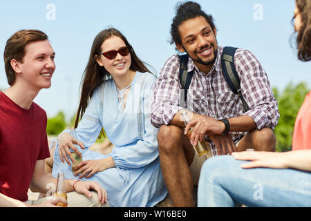 Multi-etnico gruppo di amici all'aperto in chat felicemente e bere birra mentre godendo Estate, spazio di copia Foto Stock