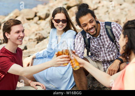 Multi-etnico gruppo di amici tintinnio di bottiglie di birra mentre godendo estate all'aperto, spazio di copia Foto Stock