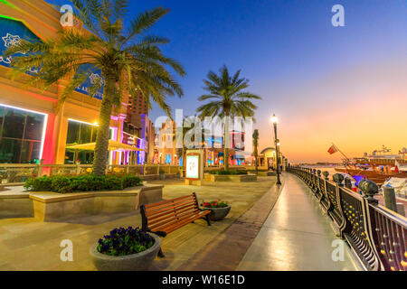 Doha, Qatar - 18 febbraio 2019:palme in passerella del porto Saudita all'Pearl-Qatar, Doha, con grattacieli di West Bay skyline al tramonto Cielo Foto Stock