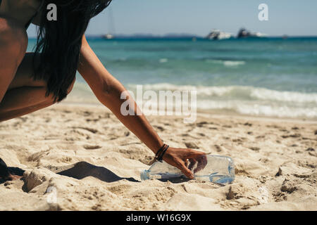 Donna di prelevare una bottiglia di acqua garbage in spiaggia. Foto Stock