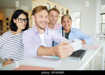 Il gruppo di allegro hipster giovani multi-etnico amici permanente al contatore con laptop e utilizzando gadget mentre si fotografa insieme nella libreria Foto Stock