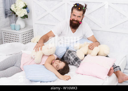 La fine della serata pazzo. Avendo divertimento pigiama party. Slumber party. Felice della paternità. Papà e una ragazza rilassante camera da letto. Pigiami stile. Padre uomo barbuto divertente ponytails di acconciatura e la figlia in pigiama. Foto Stock