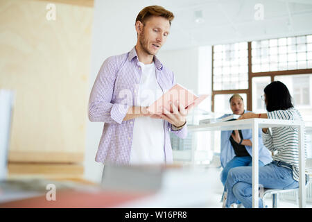 Curioso concentrato giovane con la stoppia in piedi in spaziose bookshop e leggere i contenuti del libro prima di acquistare Foto Stock