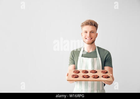 Bel maschio baker tenendo la scheda con biscotti freschi su sfondo chiaro Foto Stock