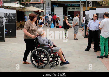 Donna anziana in una sedia a rotelle con un custode spingendo da dietro in una piazza in Granada, Spagna; fuori per una passeggiata. Foto Stock