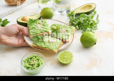 Donna tenendo la piastra con gustosi crostini di avocado dalla tabella Foto Stock