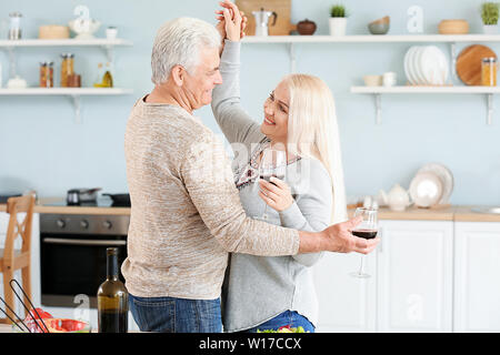 Ritratto di felice coppia matura per ballare e bere il vino in cucina Foto Stock